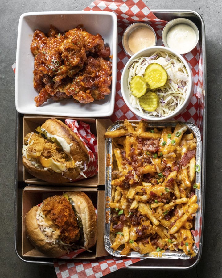 Family-style spread includes a choice of two chicken sandwiches, bacon cheese fries, boneless fried chicken bites (with a choice of soy garlic, yang-nyeom or honey garlic sauce), two mayo sauces, slaw and pickles